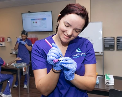 Student practicing skills at phlebotomy school, preparing a blood collection tube in a classroom setting.