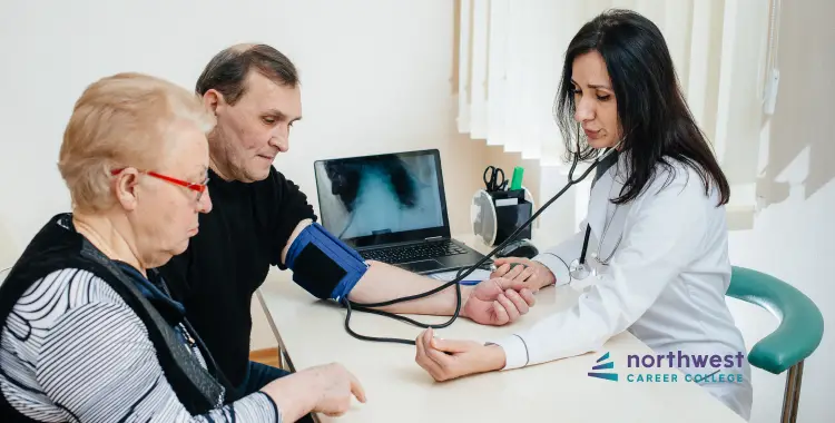 A healthcare professional checks a mans blood pressure while a woman observes in a clinical setting.
