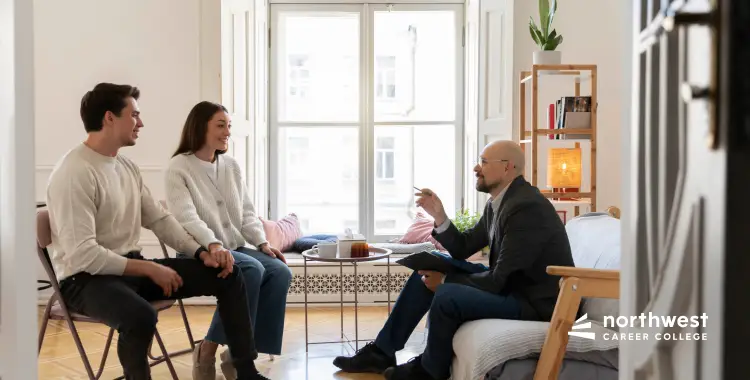 Two students and a mentor engage in a discussion in a bright, cozy room with a window and plants.