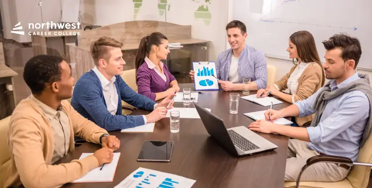 A diverse group of six people in a meeting, discussing charts and data around a conference table.