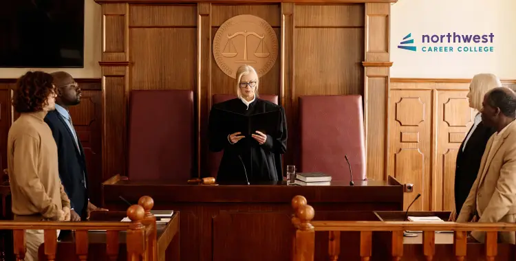 A judge addresses a group of people in a courtroom setting, with a scales of justice emblem in the background.
