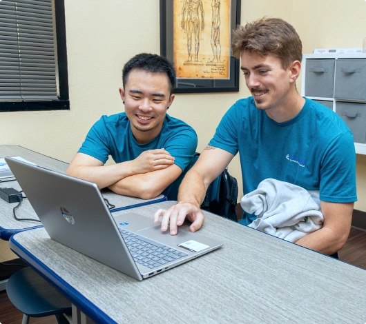 Two men in teal shirts engage in hands-on training with a laptop during BAA hands-on training in Las Vegas.