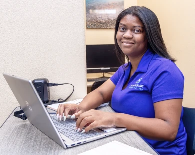 Business Administration student at class, working on a laptop with a focused expression in a study environment.