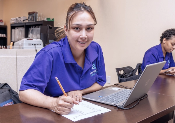 A student participates in business administrative assistant training class in Las Vegas, taking notes at a desk.
