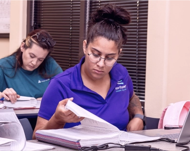 Students studying at a medical coder school, focusing on materials and taking notes in a classroom setting.
