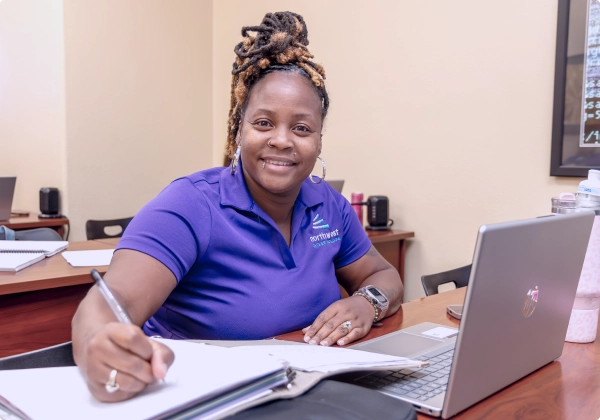 A paralegal studies program student in Las Vegas smiles while studying at her desk, taking notes beside her laptop.