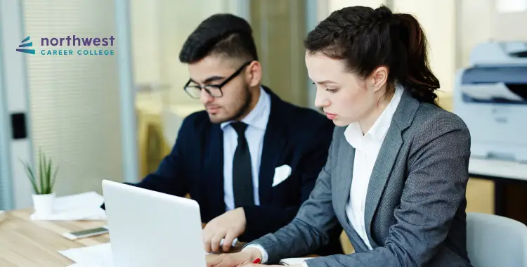 Two professionals working together at a laptop in a modern office setting.