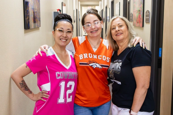 Three women pose together in a hallway, wearing sports jerseys and smiling happily.