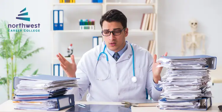 A doctor in a lab coat looks overwhelmed by stacks of paperwork in an office setting.