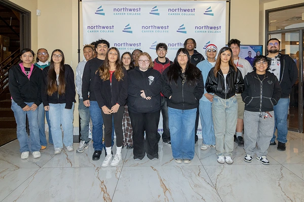 A diverse group of students poses together in front of a Northwest Career College banner.