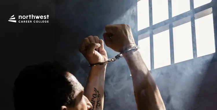 A person in handcuffs raises their arms in front of a barred window, with light streaming in.