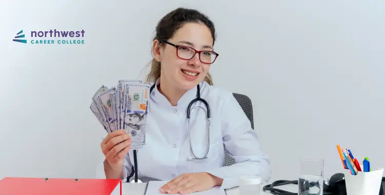 A smiling woman in a lab coat holds cash, sitting at a desk with a stethoscope and office supplies.