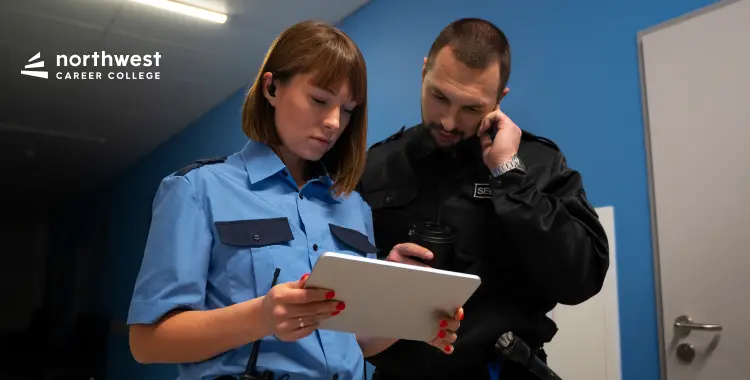 Two security personnel review information on a tablet in a hallway, one on a phone and the other focused on the screen.