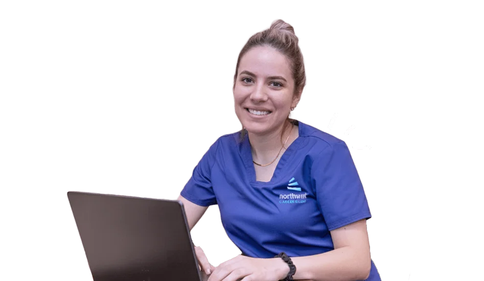 Smiling woman in scrubs studies on a laptop, representing a healthcare administration online degree program.