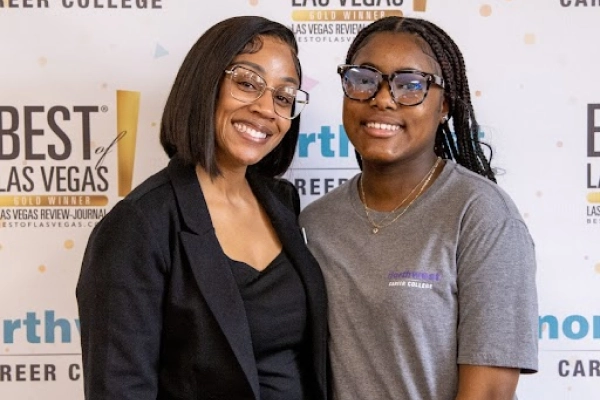 Two women smile together at an event, standing in front of a Best of Las Vegas backdrop.