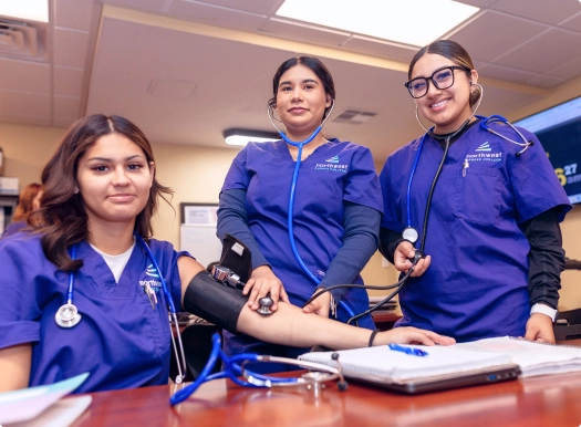 MA students with equipment practice taking blood pressure in a classroom setting, focused and engaged in learning.