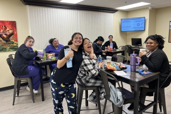 A group of smiling people enjoying snacks and drinks in a casual break room setting.