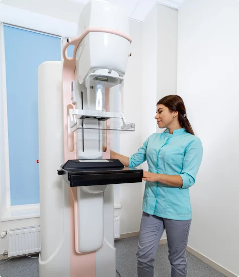 A healthcare professional adjusts a mammography machine in a bright, modern medical room.