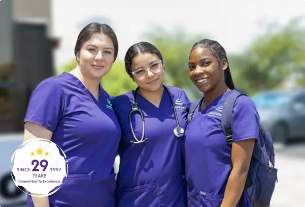Three smiling healthcare professionals in purple scrubs pose together outdoors, showcasing teamwork and dedication.